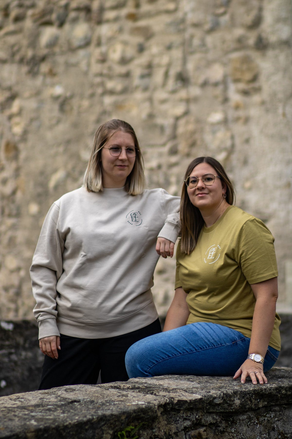 Zwei Personen im CEEL Sweatshirt Basic und im CEEL Shirt in Faded Olive vor einer alten Steinmauer