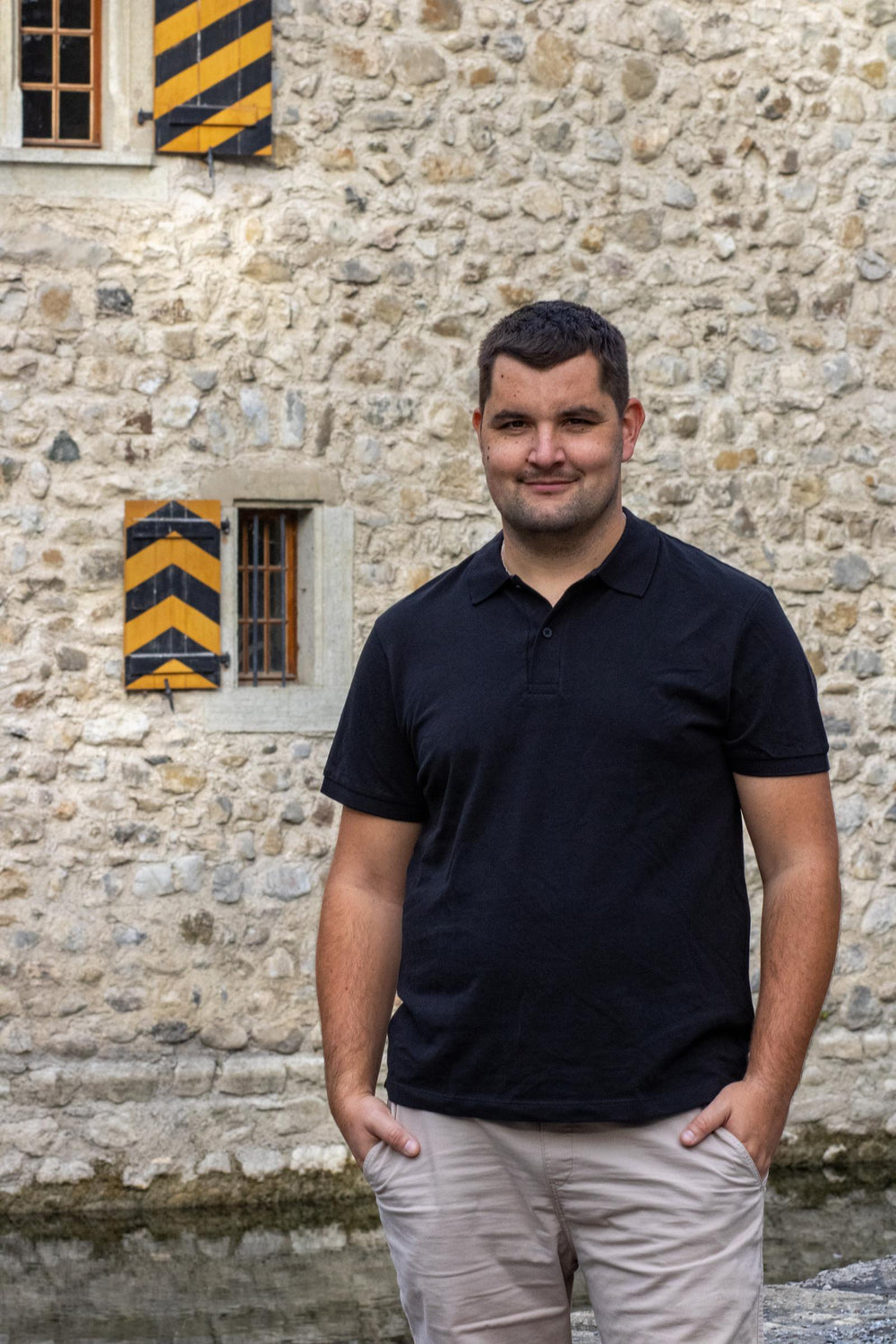 CEEL Polo Vorderansicht: Joel im schwarzen Polo vor einer Steinmauer